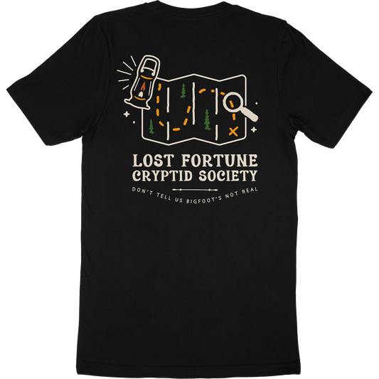 Black t-shirt that has a map and lantern artwork. The words say "Lost Fortune Cryptid Society," and "don't tell us bigfoot's not real."