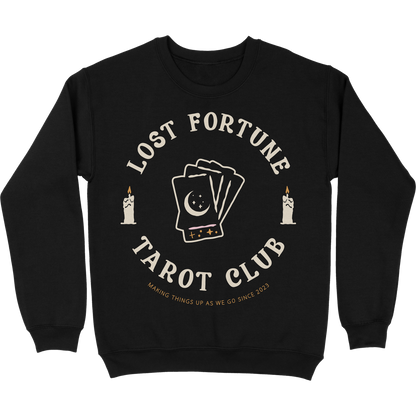 Black crewneck sweatshirt with artwork of candles and a stack of tarot cards with a moon and stars on the front. The text reads "Lost Fortune Tarot Club. Making things up as we go since 2023." 