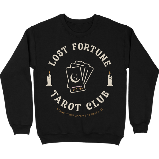 Black crewneck sweatshirt with artwork of candles and a stack of tarot cards with a moon and stars on the front. The text reads "Lost Fortune Tarot Club. Making things up as we go since 2023." 