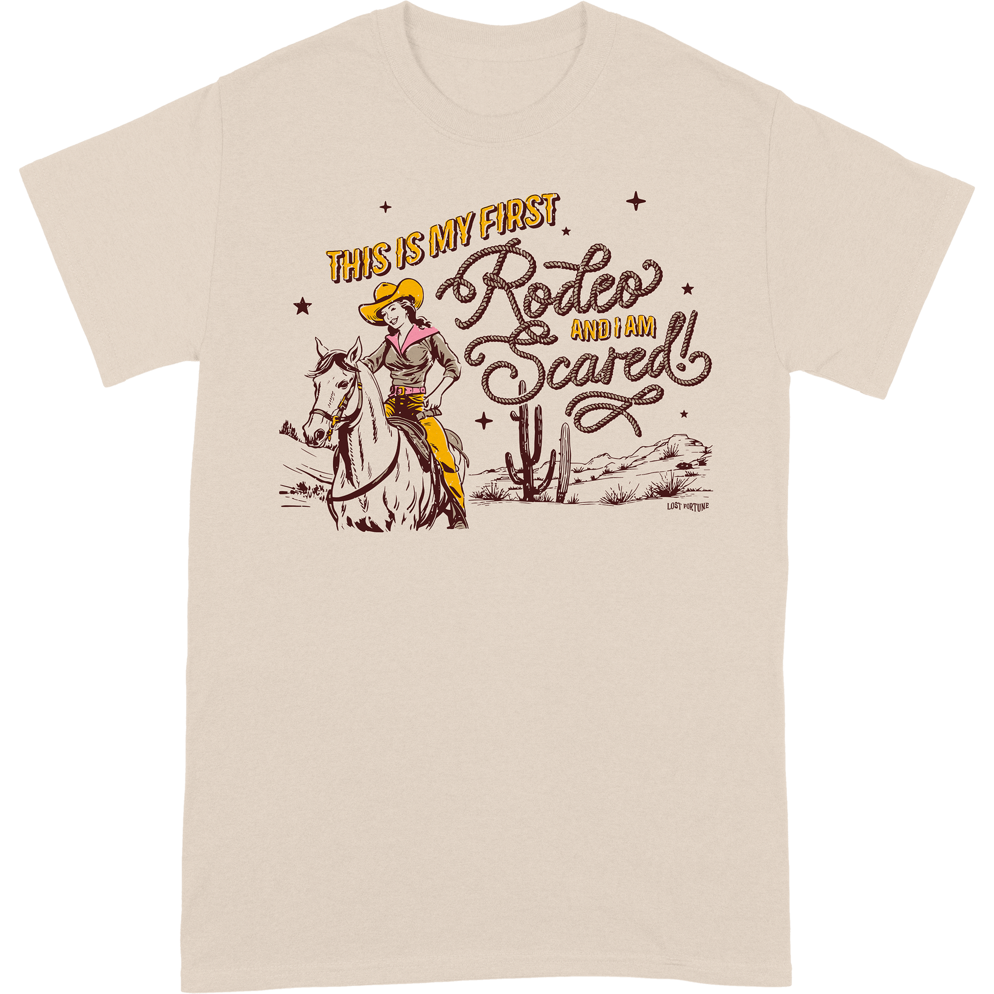 Light tan colored t-shirt that features artwork of a cowgirl riding a horse in the desert and the phrase "this is my first rodeo and I am scared"