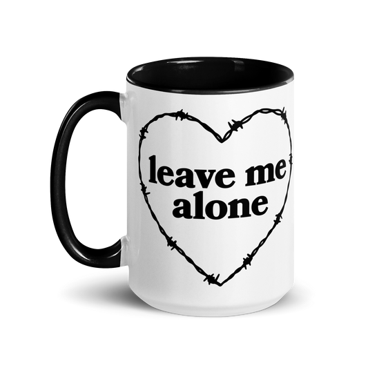 White ceramic mug with black handle and interior that features a barbed wire heart surrounding the phrase "leave me alone"