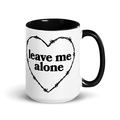 White ceramic mug with black handle and interior that features a barbed wire heart surrounding the phrase "leave me alone"